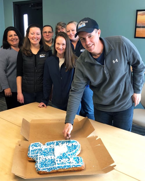 CEO Ryan Clark cuts a "42" shaped donut cake while some of the office staff look on