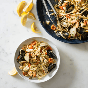 A large serving dish and a small individual bowl of linguine with calamari rings and other seafoods