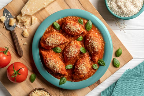 A dark green dish with stuffed calamari tubes, covered in red sauce, and sprinkled with cheese and basil leaves