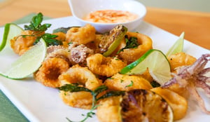 A white plate of fried calamari rings with lime wedges and dipping sauce