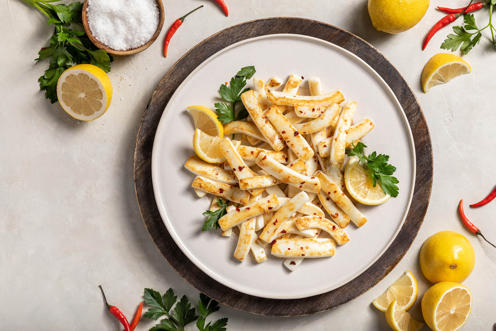 A plate of calamari strips, calamari fries, slightly seasoned and garnished with lemon and parsley